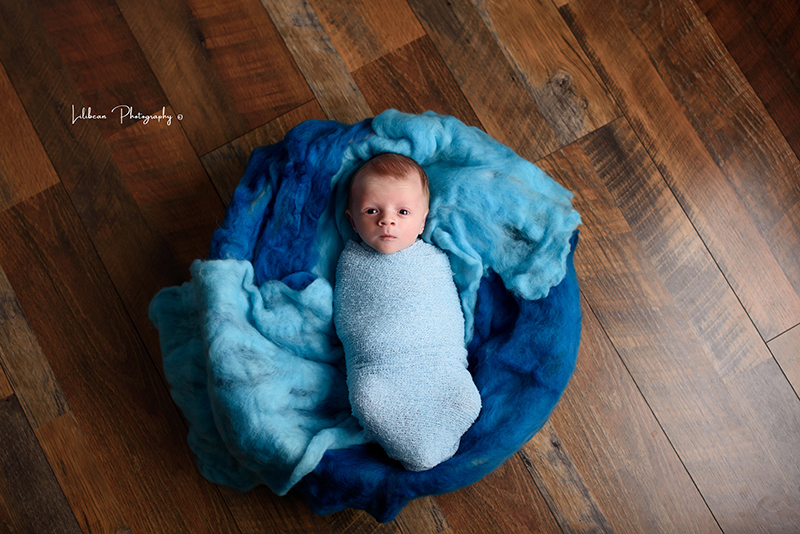 Newborn baby swaddled in blue on top of blue.