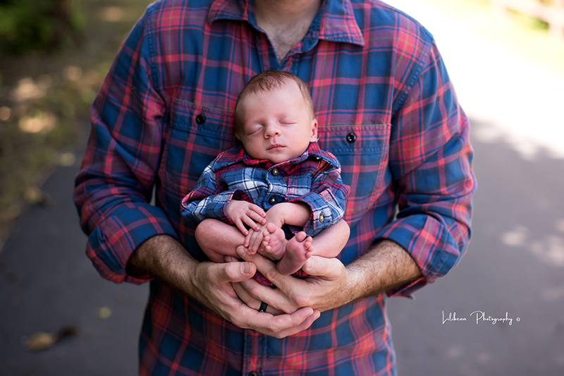 Newborn baby held by dad.  Both wearing plaid. 