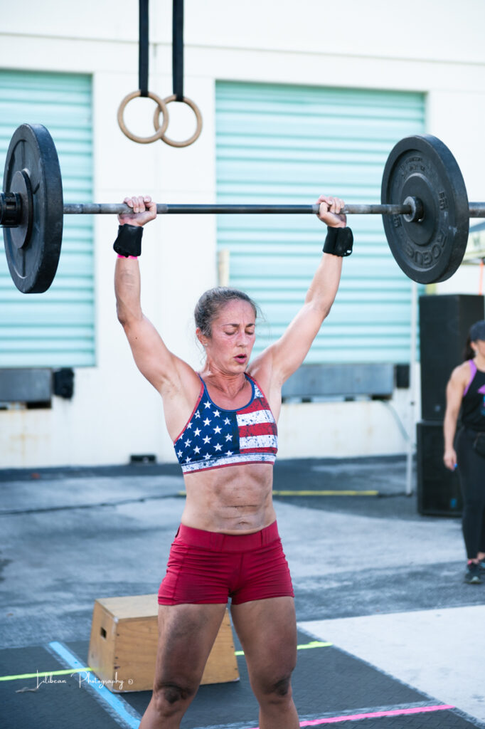 Woman lifting barbell overhead during crossfit competition